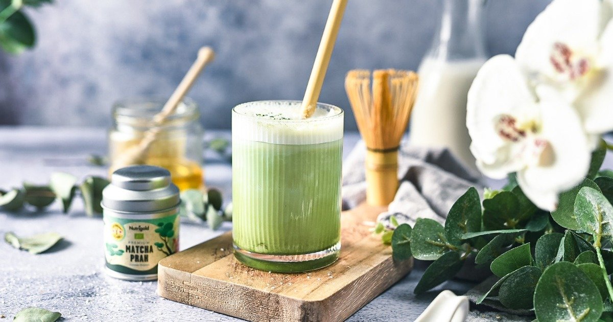 Matcha in einem durchsichtigen Becher, umgeben von Getränkezutaten