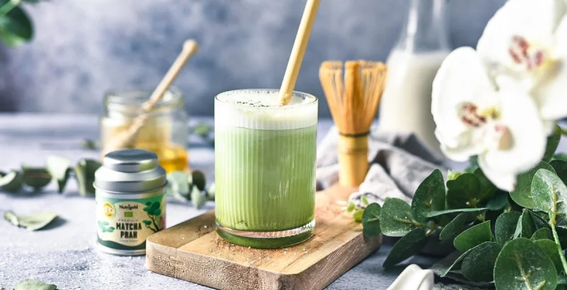 Matcha in einem durchsichtigen Becher, umgeben von Getränkezutaten