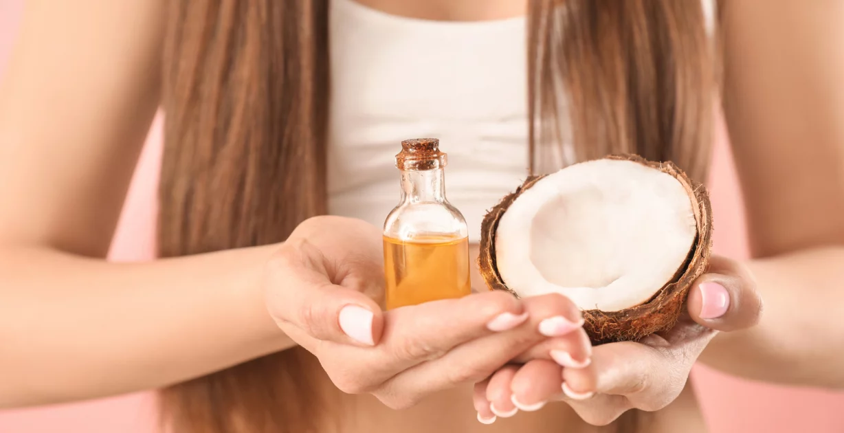 Eine halbe Kokosnuss und Kokosöl in einer Flasche in den Händen