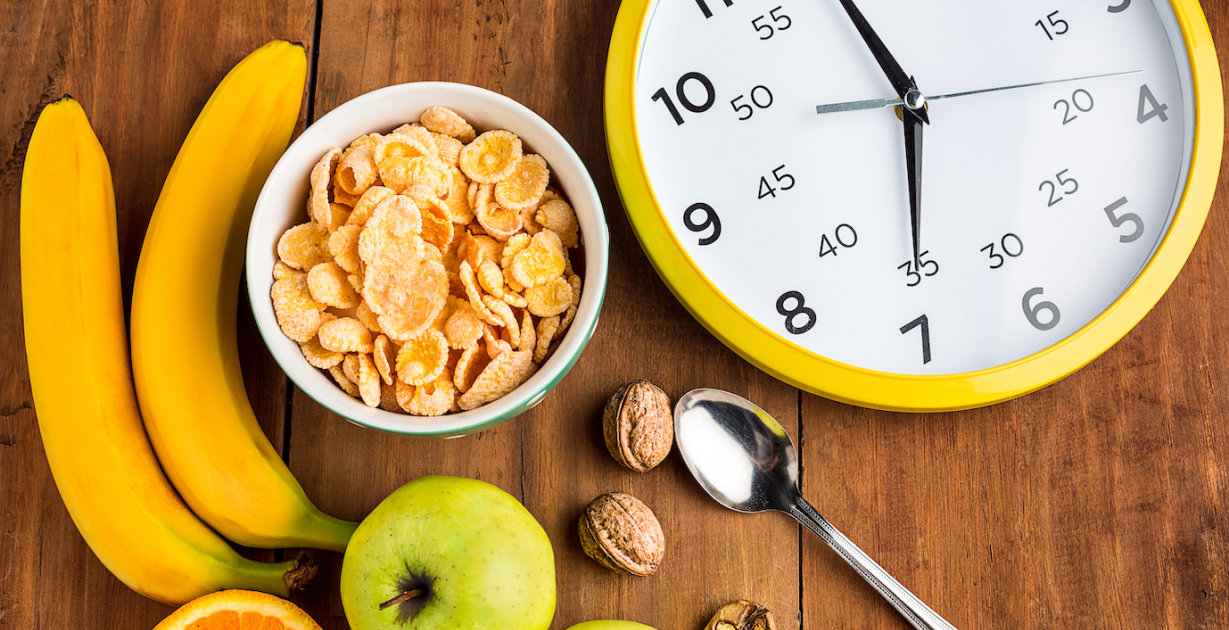 Lebensmittel und eine Uhr, die auf einem Tisch mit Obst und Cornflakes steht.