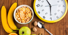 Lebensmittel und eine Uhr, die auf einem Tisch mit Obst und Cornflakes steht.