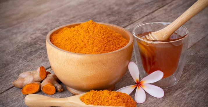 Kurkuma-Pulver in einer Holzschale, daneben eine Tasse mit Honig.